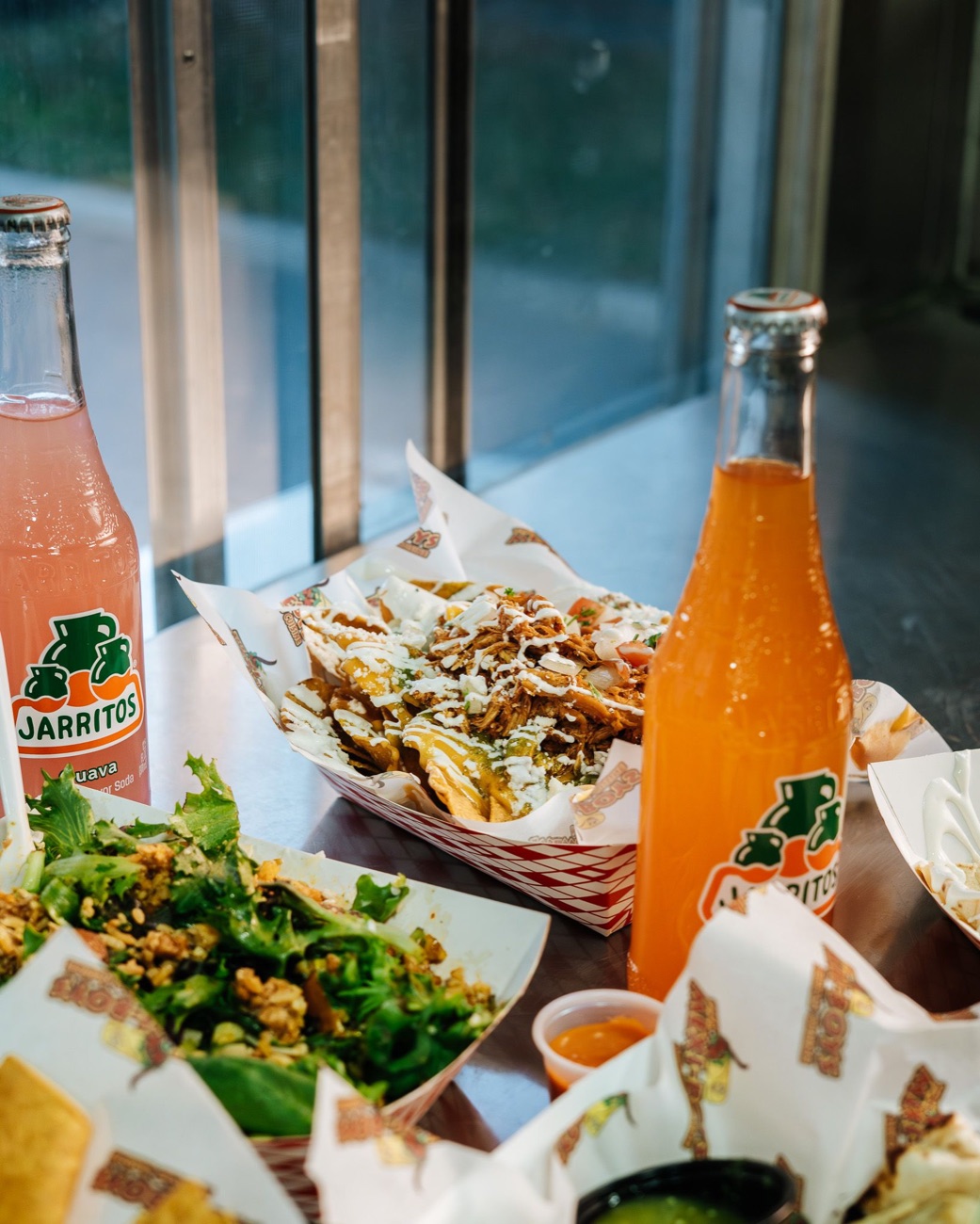Loaded nachos with cheese, protein, jalapeños, pico and crema, with Jarritos sodas
